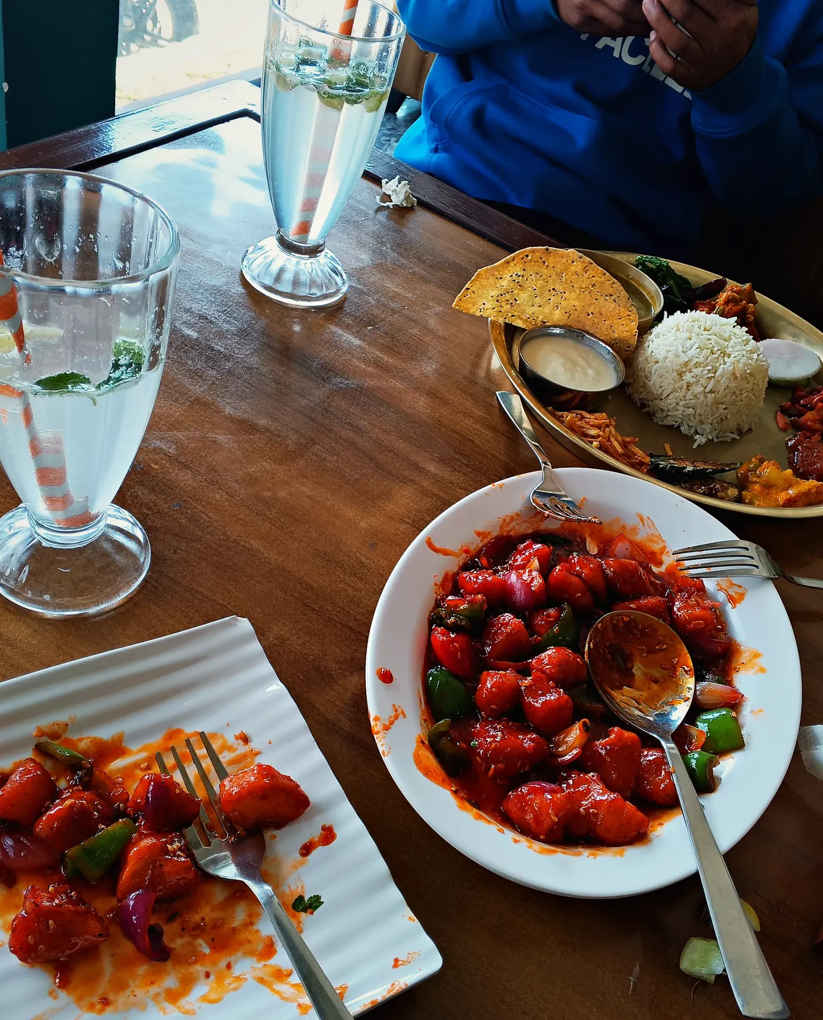 An Indo-Chinese chilli dish beside a lunch thali on a wooden table